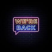 Neon sign "We're Back" against dark blue brick wall