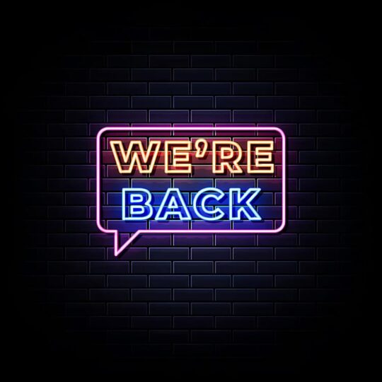 Neon sign "We're Back" against dark blue brick wall
